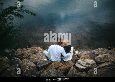 Le couple interracial est assis sur des rochers et se hale contre le fond de la rivière. Concept de relations d'amour et d'unité entre les différentes races humaines. Banque D'Images