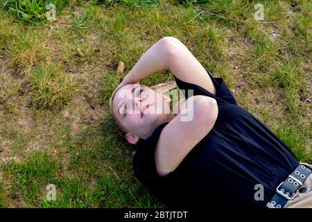 Jeune femme aux cheveux très courts se trouve dans l'herbe verte, les bras sur le cou et la tête Banque D'Images