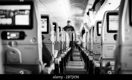 Intérieur d'un avion de passagers de grande taille avec des personnes sur les sièges et une hôtesse en uniforme marchant dans l'allée. Banque D'Images