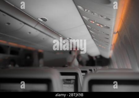 Intérieur d'un avion de passagers de grande taille avec des personnes sur les sièges et une hôtesse en uniforme marchant dans l'allée. Banque D'Images