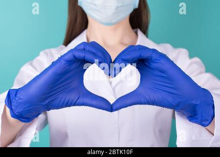 Gros plan photo de femme médecin en manteau blanc uniforme caoutchouc latex bleu gants faisant montrer le coeur avec ses mains isolées sur bleu sarcelle turqu Banque D'Images