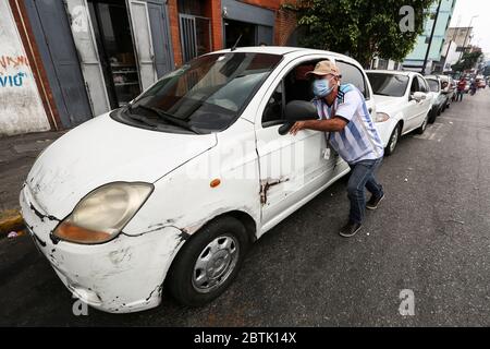 Caracas, Venezuela. 26 mai 2020. Un homme avec un masque pousse sa voiture, qui est dans une longue file d'attente, à une station-service au milieu d'une pénurie continue de carburant. Le Venezuela possède d'énormes réserves de pétrole, mais en raison d'un manque de capacité de raffinage, il a beaucoup trop peu d'essence. Les voitures sont actuellement autorisées à remplir jusqu'à 30 litres de carburant. Selon les informations iraniennes, le premier de plusieurs pétroliers iraniens avec de l'essence pour le Venezuela devrait avoir atteint le pays sud-américain d'ici la fin mai 2020. Crédit : Pedro Rances Mattey/dpa/Alay Live News Banque D'Images