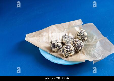 Cinq boules d'énergie faites maison dans du papier d'emballage sur une table bleue. Un dessert au chocolat maison sain pour le petit déjeuner vous remplira d'énergie. Arrosage d'écrous Banque D'Images