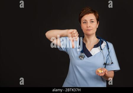 Mécontentement la médecin européenne montre un signe de désapprobation, garde le pouce vers le bas, exprime le mécontentement, fronces de sourcils face au mécontentement, isolé sur fond noir. Concept de langage corporel. Banque D'Images