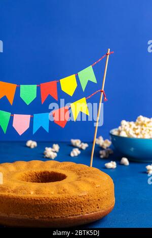 Tarte au maïs avec drapeaux multicolores. Sucreries brésiliennes et pop-corn sur une table bleue. Drapeaux de fête de Festa junina Banque D'Images