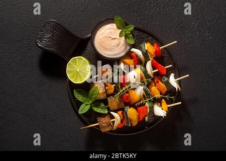 kebabs vegan prêts de légumes et tofu fumé avec sauce cajou et paprika fumé sur fond noir Banque D'Images