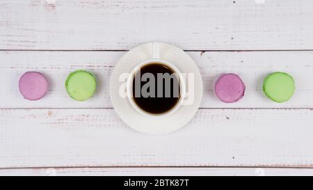 Macarons colorés et une tasse de café sur fond de bois, plat de gros plan. Concept de petit déjeuner. Copier l'espace. Banque D'Images