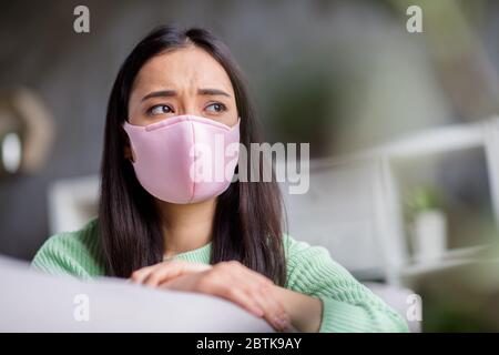 Photo de la maison triste virus corona malade patient asiatique femme assis canapé regarder fenêtre rêveuse manquant aller à l'extérieur garder l'auto-isolement social Banque D'Images