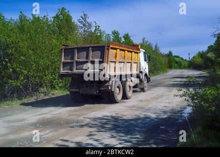 Un camion-benne roule sur une route de terre sur fond de forêt et de ciel bleu. Banque D'Images