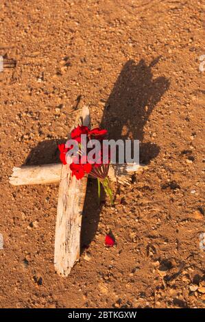 Image d'une croix faite de deux branches d'arbre sèches à côté de quelques fleurs rouges comme signe de deuil et de reconnaissance de quelqu'un qui est mort Banque D'Images