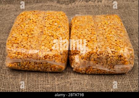 Petits pois jaunes dans un sac de cellophane sur fond de toile de jute à texture grossière. Grains traditionnels pour la préparation de soupes et de porridges. Gros plan Banque D'Images