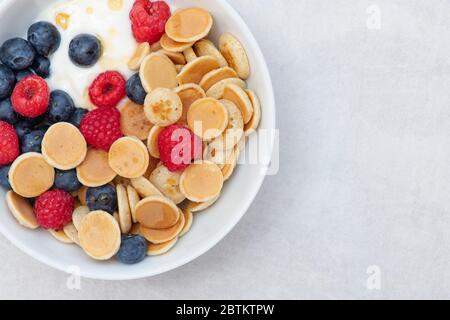 Bol de mini crêpes aux céréales faites maison avec yaourt aux myrtilles framboises et sirop d'érable Banque D'Images