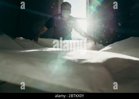 Homme asiatique nettoyant le lit le matin. L'action de la maison. La chambre est baignée de lumière. Banque D'Images