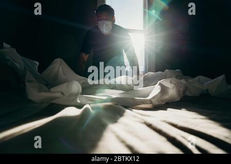 Homme asiatique nettoyant le lit le matin. L'action de la maison. La chambre est baignée de lumière. Banque D'Images