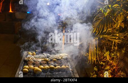 Brochettes de pommes de terre et poisson grillés dans du papier aluminium avec fumée du gril. Fête barbecue. Banque D'Images