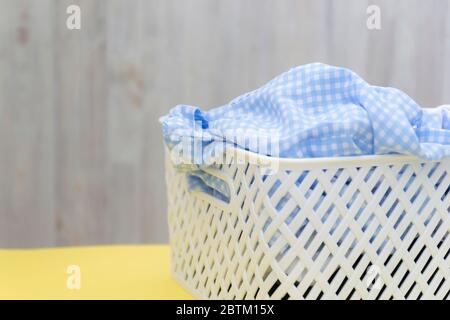 Chemises blanches bleues vierges dans un panier en plastique blanc sur une table jaune sur fond gris. Blanchisserie, nettoyage à la maison, propreté et fraîcheur Banque D'Images