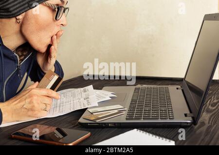 Une femme européenne frustrée tenant une carte bancaire, regardant un ordinateur portable, facture, calculant ses dépenses mensuelles, dettes à la maison. Crise économique. Femme en faillite Banque D'Images