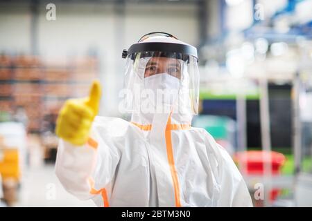 Travailleur avec masque de protection et combinaison dans l'usine industrielle, mouvement de la main vers le haut. Banque D'Images