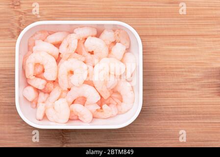 Crevettes cuites dans un bol blanc sur une planche à repasser en bois, vue du dessus Banque D'Images