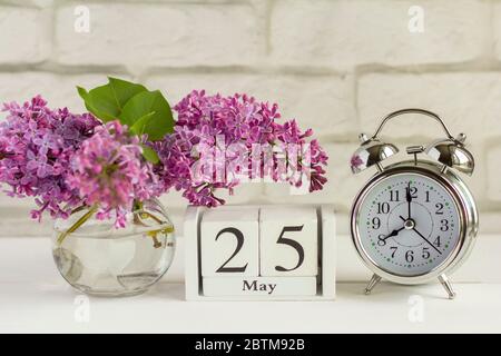 Mai 25 sur un calendrier en bois à côté du bouquet de lilas réveil.un jour du mois de printemps.fin de l'année scolaire.la dernière cloche dans les écoles. Banque D'Images