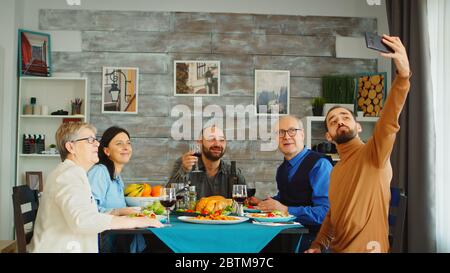 Beau barbu homme utilisant son smartphone pour prendre un selfie avec sa famille au dîner. Banque D'Images