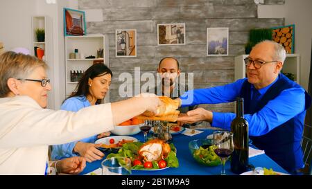 Homme dans les années soixante servant sa femme avec du pain au dîner en famille. Banque D'Images