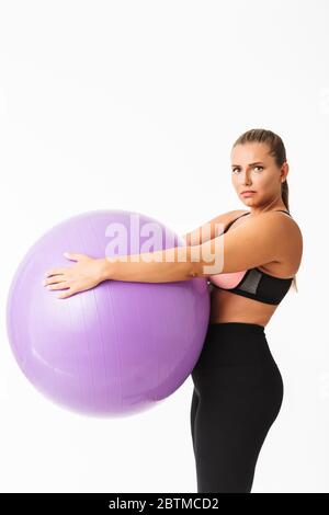 Jeune femme plousse tenant le ballon de fitness dans les mains malheureusement regardant dans l'appareil photo sur fond blanc isolé Banque D'Images