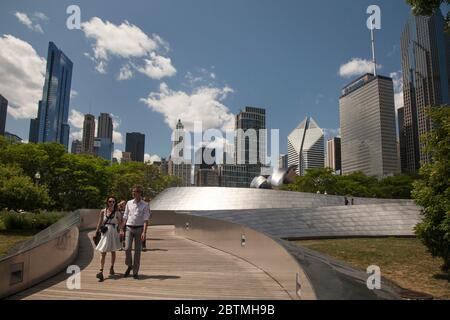 Photo horizontale d'un couple traversant le pont piétonnier Frank Gehry BP, avec les gratte-ciel de Chicago comme arrière-plan, Millenium Park, Illinois, États-Unis Banque D'Images