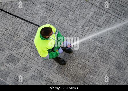 Un travailleur tenant un tuyau pour nettoyer le trottoir avec de l'eau. Entretien urbain ou concept de nettoyage Banque D'Images