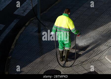 Un travailleur tenant un tuyau pour nettoyer le trottoir avec de l'eau. Entretien urbain ou concept de nettoyage Banque D'Images