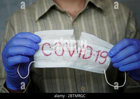 suppression du masque, fin de la quarantaine. Arrière-plan Covid-19. Arrêter la propagation et éliminer le coronavirus. Pandémies. Mains dans des gants médicaux bleus déchirant le masque Banque D'Images