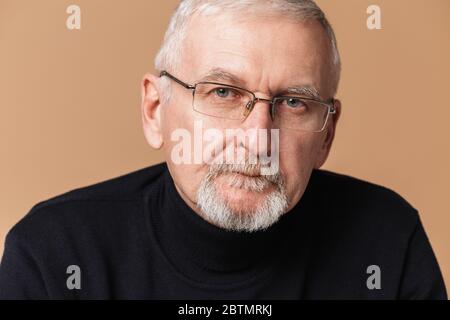 Homme beau et vieux avec cheveux gris et barbe en lunettes et chandail regardant avec soin dans l'appareil photo sur fond beige isolé Banque D'Images