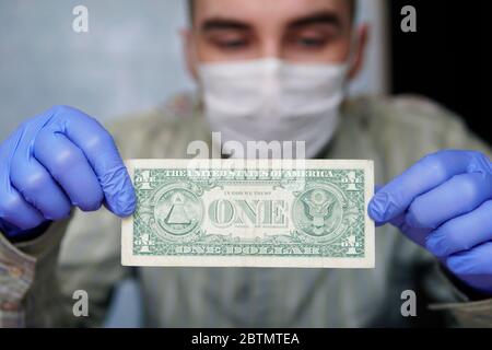 Virus argent. L'homme en gants de protection compte des billets de dollars américains. La santé et la protection des mains contre les virus, les germes et les bactéries pendant l'épidémie de grippe covid Banque D'Images