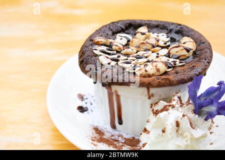 Brownies avec garniture aux amandes et crème fouettée dans une tasse blanche sur une table en bois. Banque D'Images