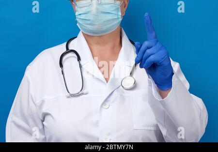 la femme médecin a soulevé l'index de sa main gauche, geste d'attention, fond bleu Banque D'Images