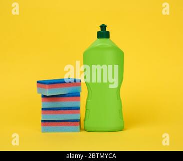 éponges rectangulaires bleues pour le lavage de la vaisselle et bouteille en plastique vert avec détergent, fond jaune Banque D'Images