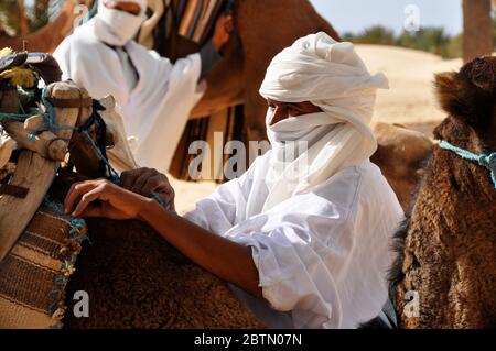 Un tunisien en costume traditionnel turban blanc se prépare à faire une balade à dos de chameau dans le désert saharien en Tunisie, en Afrique. Format paysage. Banque D'Images