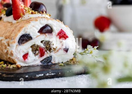 Rouleau de meringue avec baies de pralines à la pistache fraîches et crème fouettée et crème au fromage caillé. Dessert d'été Banque D'Images