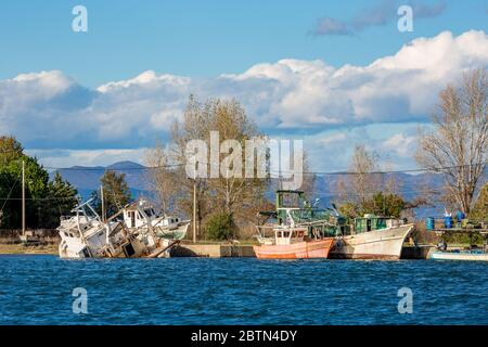 Peu de bateaux de pêche abandonnés au début de l'hiver au port de Fanari, région de Xanthi, dans le nord de la Grèce. Eaux bleues cristallines, ciel bleu ciel nuageux et chaîne de montagnes en arrière-plan Banque D'Images