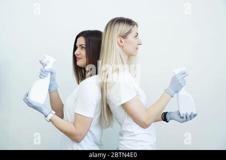 Deux femmes tiennent une bouteille vaporisée avec un antiseptique ou un détergent comme des pistolets. Concept de santé ou de nettoyage Covid-2019, sur fond blanc Banque D'Images