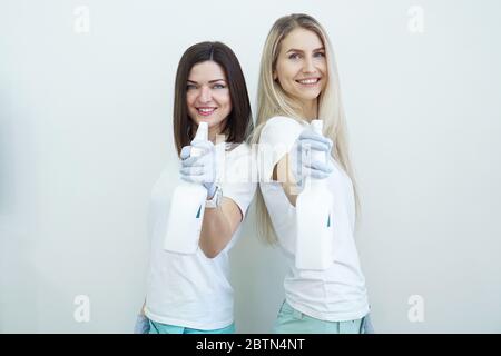 Deux femmes tiennent une bouteille vaporisée avec un antiseptique ou un détergent comme des pistolets. Concept de santé ou de nettoyage Covid-2019, sur fond blanc Banque D'Images