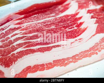 Gros plan de tranches de bacon cru sur un plateau blanc servant à préparer de délicieux plats dans la cuisine. Vue horizontale Banque D'Images