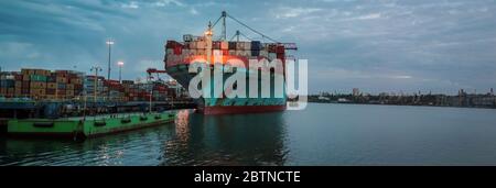 Chargement du navire-conteneur dans le port maritime au crépuscule. Logistique et transport du conteneur navire de cargaison avec pont de grue de travail dans le chantier naval, logistique Banque D'Images