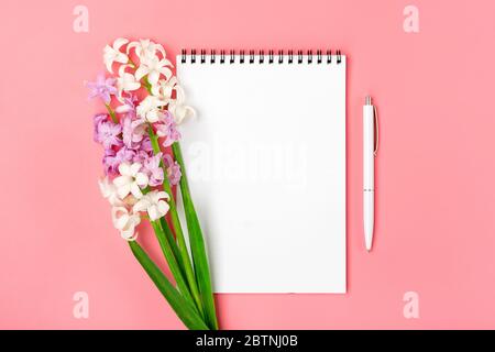 Cahier blanc ouvert, stylo, bouquet de fleurs jacinthes sur fond rose Flat Lay vue du dessus espace copie maquette Banque D'Images