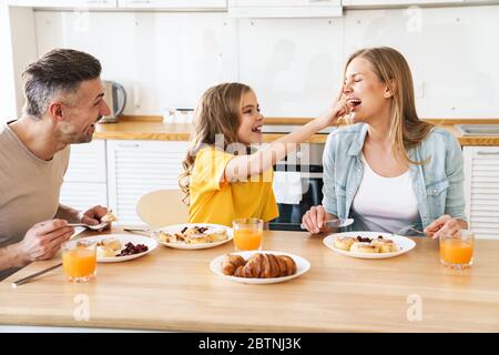 Photo de caucasien drôle belle famille riant tout en prenant le petit déjeuner dans la cuisine moderne Banque D'Images