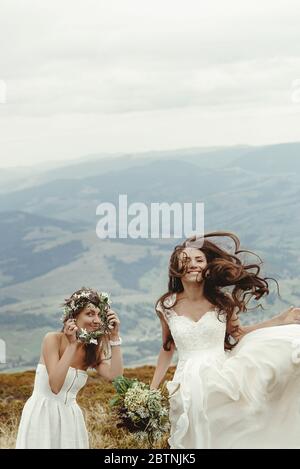 demoiselle d'honneur et superbe mariée ayant plaisir et saut, mariage de boho, cérémonie de luxe à la montagne Banque D'Images