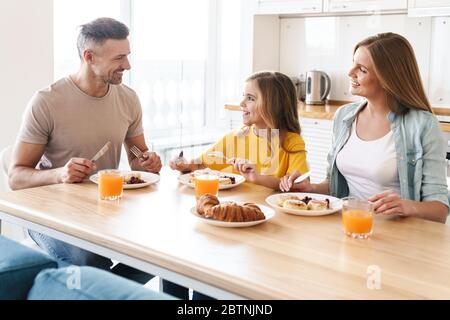 Photo de la bonne famille caucasienne souriant et parlant tout en prenant le petit déjeuner dans la cuisine moderne Banque D'Images