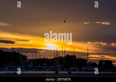 PORTO LAGOS, GRÈCE - 29 NOVEMBRE 2019: Le soleil est magnifiquement situé au-dessus des yachts et des bateaux amarrés. Coucher de soleil doré orange sur le port de Porto Lagos, région de Xanthi, Grèce du Nord Banque D'Images