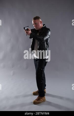 Image isolée d'un homme avec un pistolet portant une veste en cuir noir. Idéal pour les applications de couverture ou de détection telles que la conception de couverture de livre et d'ebook. Banque D'Images