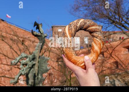 Femme tenant la main de l'Obwarzanek krakowski - le fameux bagel de Cracovie avec graines de pavot et sésame. Le dragon de Wawel en arrière-plan. Image horizontale Banque D'Images
